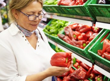 Foto von Frau mit Paprika in der Hand vor Gemüseregal im Supermarkt