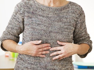 Foto von älterer Frau, die sich vor Schmerzen den Bauch hält